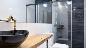 A modern bathroom with a black vessel sink, a wooden countertop, a white toilet, and a glass-enclosed shower area. - Madrid Experience - 3-Bedroom Apartment in the City Center (Madrid)