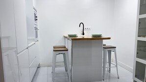 A compact kitchen with a central island, two stools, and a white cabinet with glass doors. - Madrid Experience - 3-Bedroom Apartment in the City Center (Madrid)