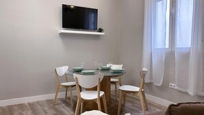 A dining area with a round table, white chairs, and a flat-screen TV mounted on the wall. - Madrid Experience - 3-Bedroom Apartment in the City Center (Madrid)