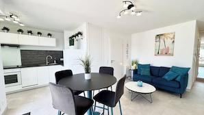 A modern kitchen with white cabinets, a black countertop, and a dining area with a round table and chairs. - T2 contemporain - Balcon - Vue mer panoramique (Guidel)