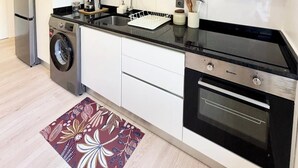 Eine moderne Küche mit weißen Schränken, einem Edelstahl-Kühlschrank, einer eingebauten Mikrowelle, einer Waschmaschine und einem Backofen.