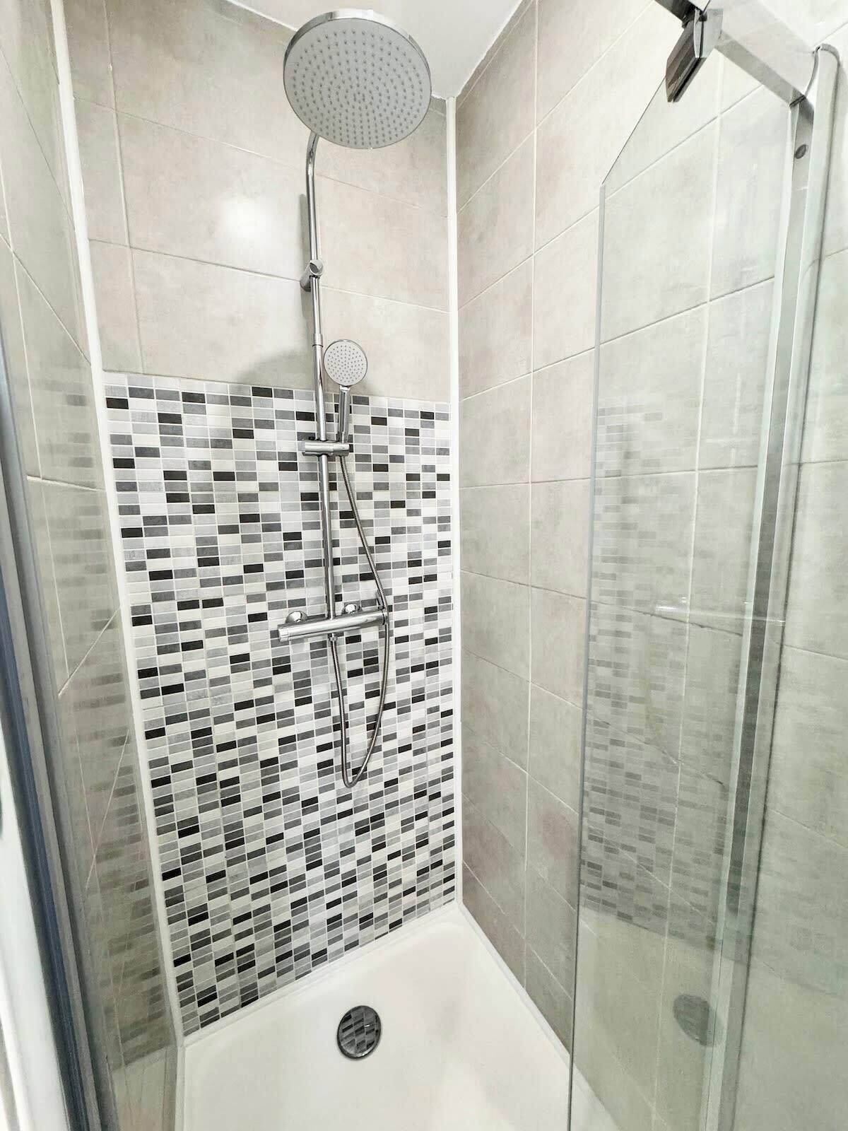A shower with a glass door and a tiled wall with a mosaic pattern.