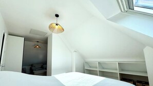 Une chambre avec un grand lit, une lucarne, un luminaire suspendu et une bibliothèque intégrée.