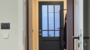 Ein Gang, der zu einer dunklen Tür mit Fenster, Lichtschalter und Thermostat an der Wand führt.