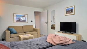 Ein Hotelzimmer mit einem Bett, einem Sofa, einem Fernseher, einem kleinen Tisch und zwei gerahmten Bildern an der Wand.