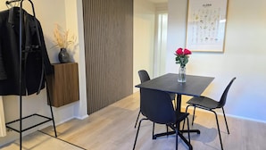 Ein moderner Essbereich mit einem Holztisch, schwarzen Stühlen und einer Vase mit roten Blumen.