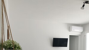 A modern living room with a grey sofa, a small round table with a plant, and a mounted TV on the wall. - Nel cuore di Milos (Milos)