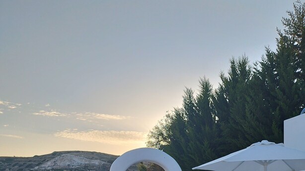 A terrace with white furniture, a pergola, and a view of the landscape. - Nel cuore di Milos (Milos)
