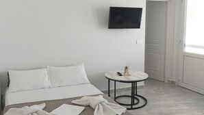 A hotel room with a bed, a small round table, a TV mounted on the wall, and a window with curtains. - Nel cuore di Milos (Milos)