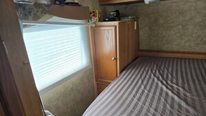 Une chambre à coucher de taille modeste, avec un lit simple, une armoire en bois et une fenêtre équipée de stores.