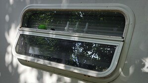Une fenêtre munie d’un moustiquaire, d’une petite grille d’aération et d’une prise électrique.