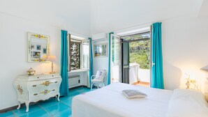 Ein Schlafzimmer mit Bett, Kommode, Stuhl und einem Balkon mit Vorhängen.