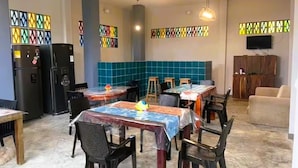 A dining area with tables covered in plastic, chairs, a refrigerator, a television, and a blue tiled wall. - Family Studio Apartment Near the Sea - Coveñas (Coveñas)