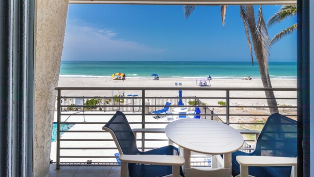 Uma varanda com vista para a praia, uma piscina e cadeiras de praia.