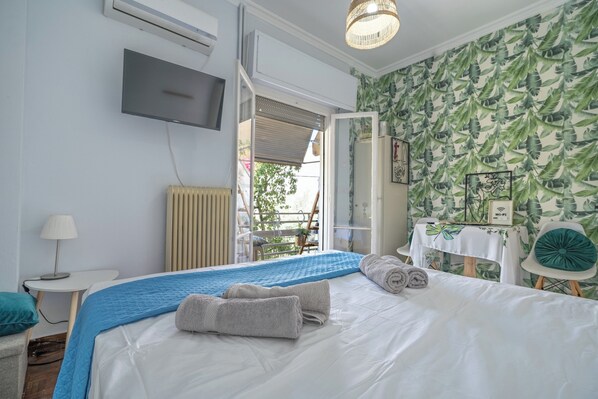 A hotel room with a bed, a TV, a table with a white tablecloth, and a view of the outdoors.
