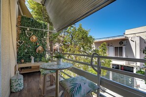 A balcony with a round table and two chairs, a green leafy wall decoration, and a potted plant.