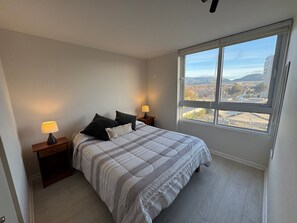 Un dormitorio con un ventanal grande, una cama con ropa de cama a rayas, dos lámparas de noche y vistas a un paisaje urbano.