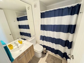 Un baño con lavamanos blanco, inodoro, espejo y cortina de ducha a rayas horizontales.