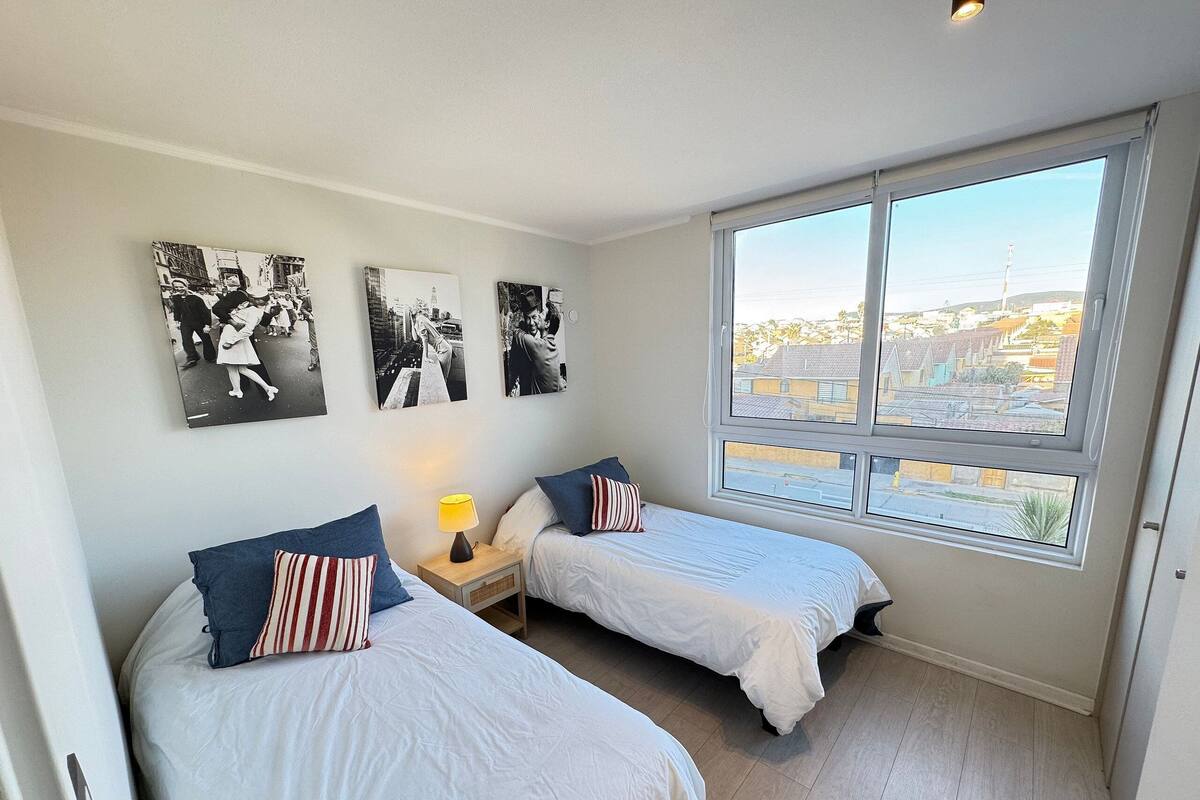 Une chambre avec deux lits, une table de chevet, une lampe et trois photographies en noir et blanc accrochées au mur.
