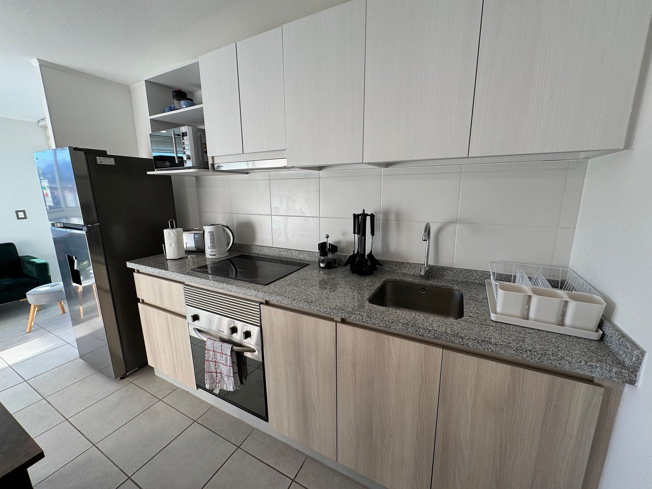 A modern kitchen with a built-in oven, a sink, and a countertop with a kettle and coffee maker.