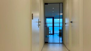 Un couloir qui donne sur une pièce dotée d’une grande fenêtre et d’un fauteuil.
