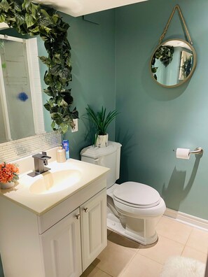 Bathroom features a modern sink, toilet, and mirror with a wooden frame, complemented by two potted plants.