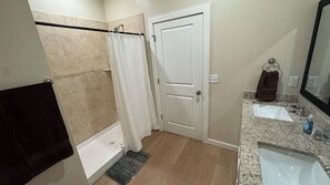 Ein Badezimmer mit Badewanne, Duschvorhang, Tür, Waschbecken und Spiegel.