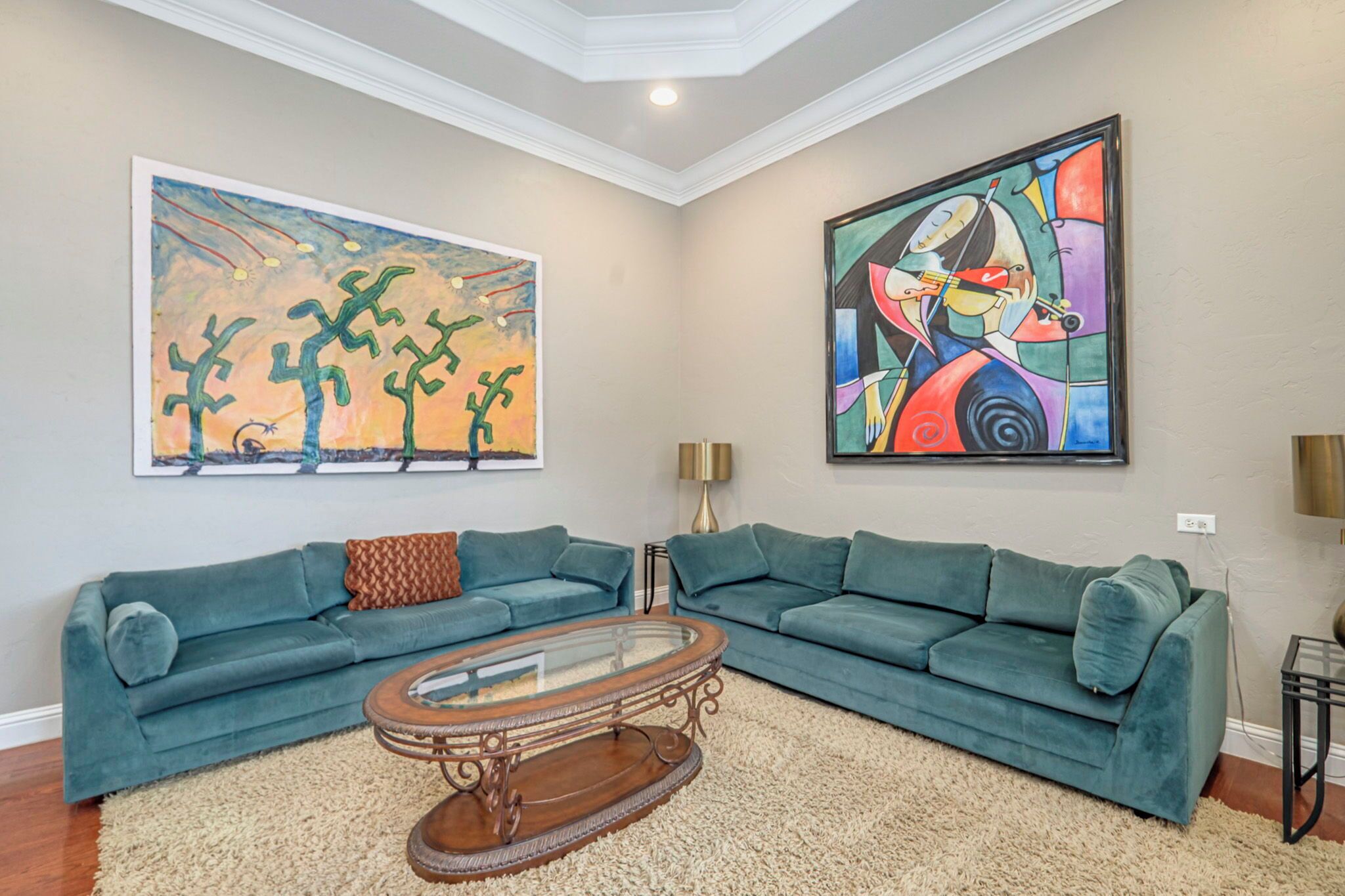 A living room with two teal sofas, a glass coffee table, and two large abstract paintings on the walls.