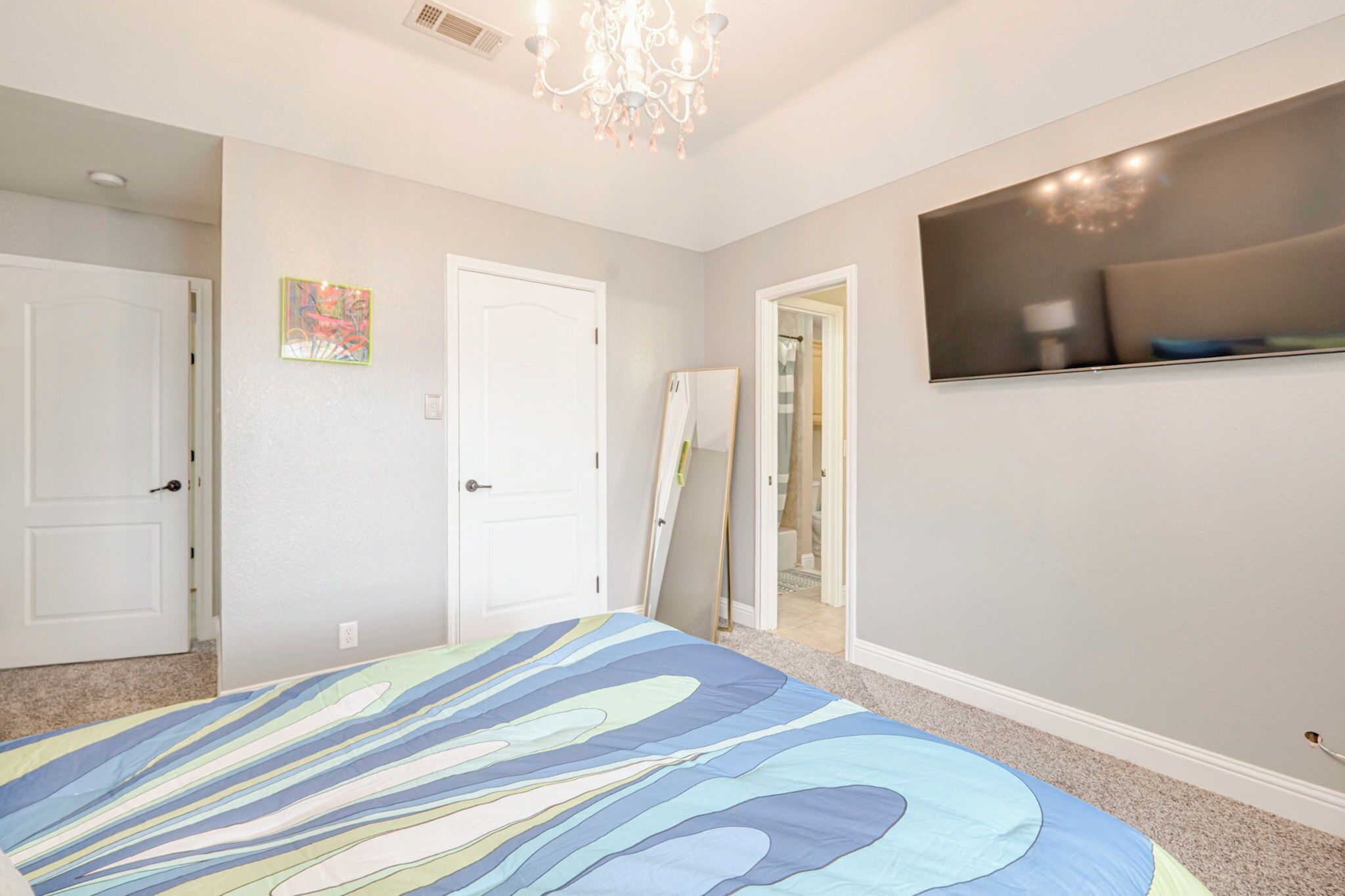 A bedroom with a large bed, a chandelier, a painting, and a TV on the wall.
