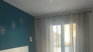 Une chambre à coucher avec un lit, une table de chevet, une horloge murale et une fenêtre avec des rideaux.