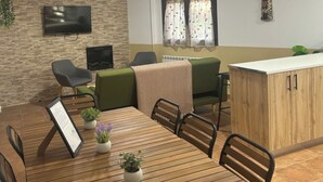 Un coin repas avec une table en bois, des chaises et une petite plante en pot. Un téléviseur est fixé au mur et il y a une fenêtre avec des rideaux.