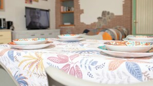 A dining table with colorful plates and a floral tablecloth, set in a room with a TV, bookshelves, and a green door. - Il Cortiletto  (Agerola)