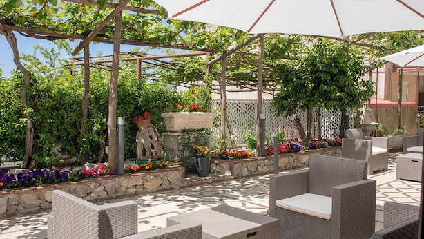 An outdoor patio with wicker furniture, a pergola, and a variety of potted plants and flowers. - Il Cortiletto  (Agerola)