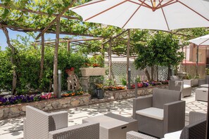 An outdoor patio with wicker furniture, a pergola, and a variety of potted plants and flowers. - Il Cortiletto  (Agerola)