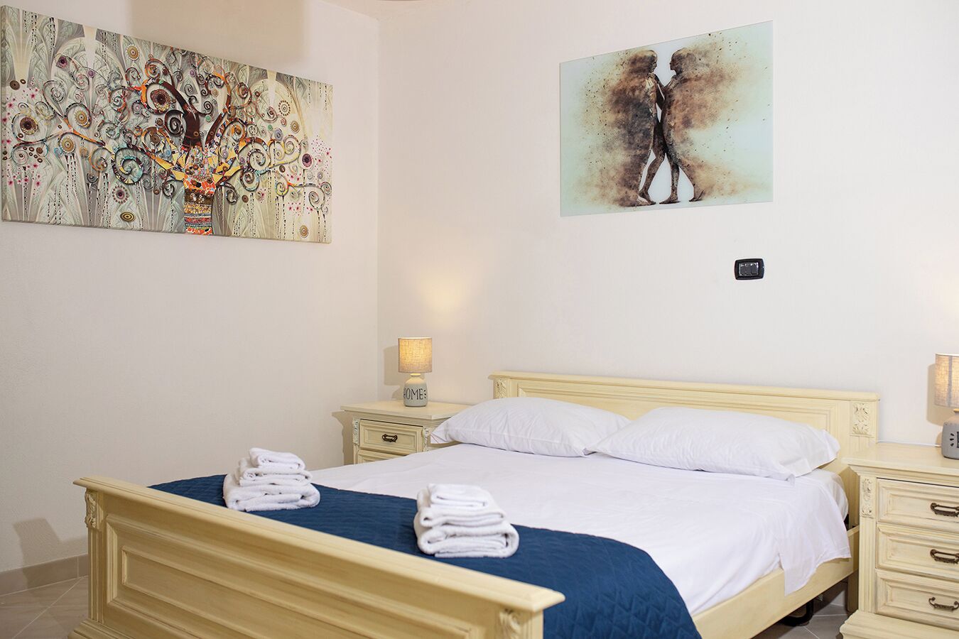 A bedroom with a bed, two bedside tables, a nightstand, and two wall-mounted lamps.
