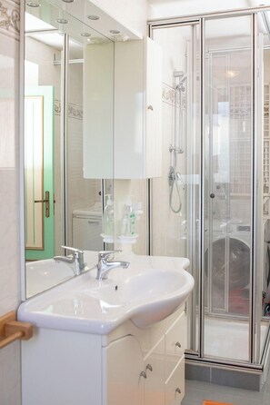 Ein modernes Badezimmer mit einem weißen Waschbecken, einer Duschkabine aus Glas und einem Schminktisch mit Spiegel.