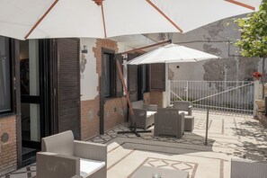Eine Terrasse im Freien mit Korbmöbeln, einem weißen Sonnenschirm und einer Ziegelwand.