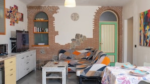 A cozy living room with a sofa, a coffee table, and a TV. There is a bookshelf and a door with a unique arch design. - Il Cortiletto  (Agerola)
