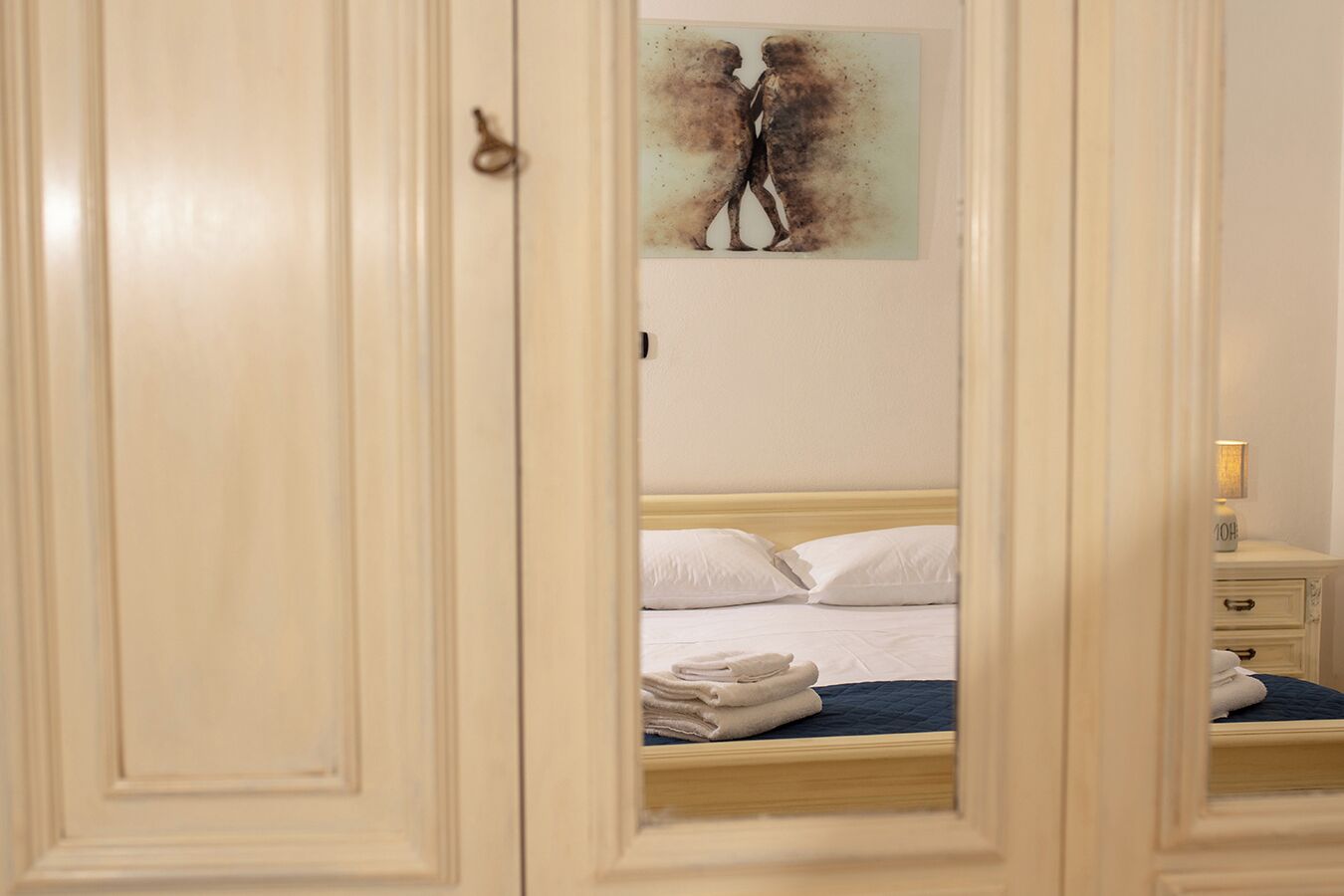 Een slaapkamer met een bed, kussens, een nachtkastje en een kunstwerk aan de muur.