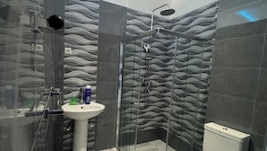 A modern bathroom with a glass-enclosed shower, a pedestal sink, and a toilet with a patterned seat. - Mangungumete Motel (Magungumete)
