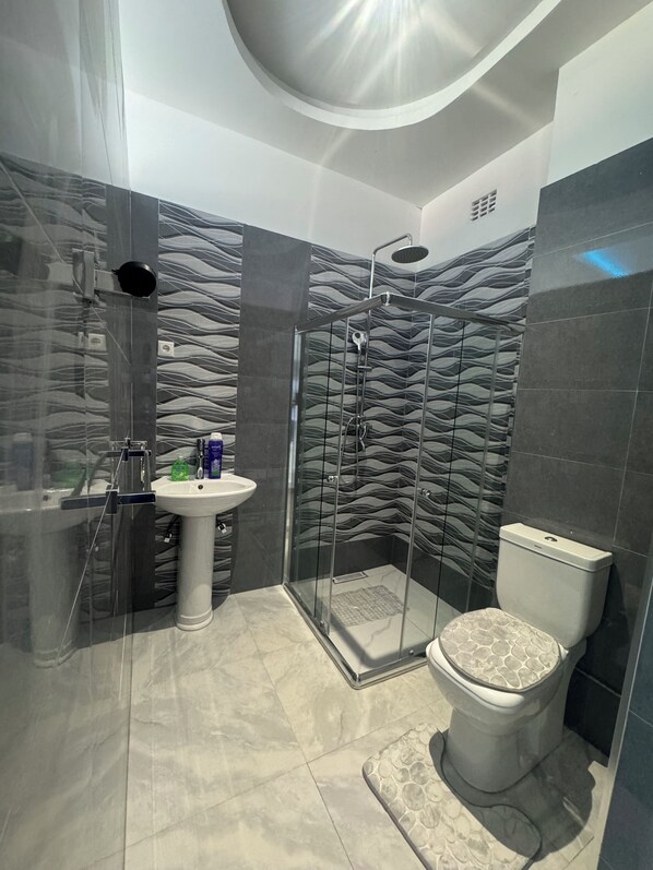 A modern bathroom with a glass-enclosed shower, a pedestal sink, and a toilet with a patterned seat.