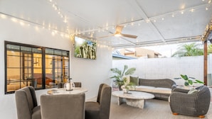 Ein möblierter Außenbereich mit einer Terrasse, Deckenventilator, Lichterketten, einem großen Fenster und einer Couch.
