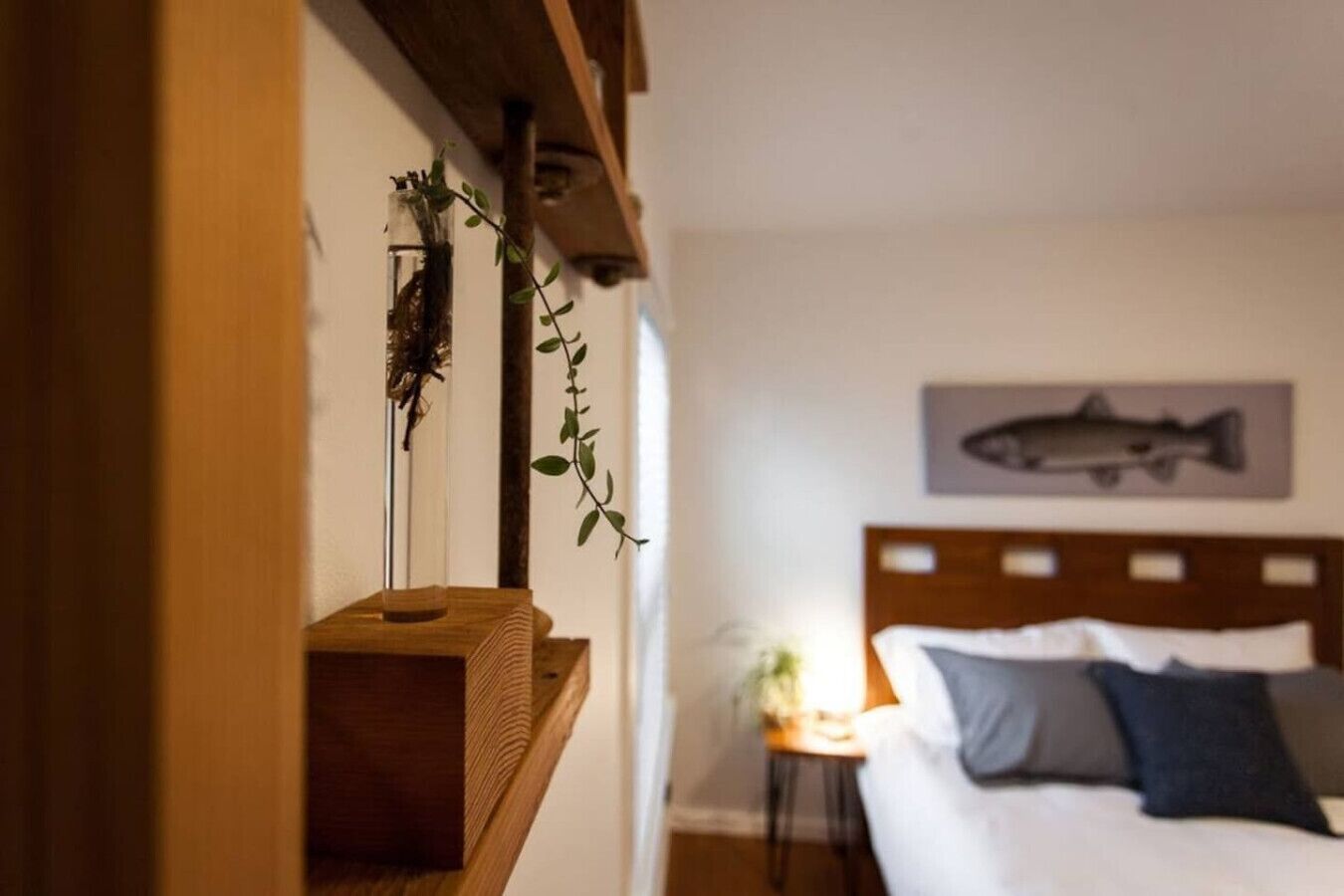 Una camera da letto con una testiera in legno, un letto con cuscini, un comodino con una lampada e un’illustrazione di un pesce appesa al muro.