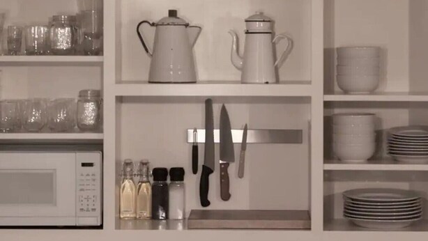 Una cocina con armarios blancos, un microondas, una cafetera, un hervidor y varios utensilios de cocina.