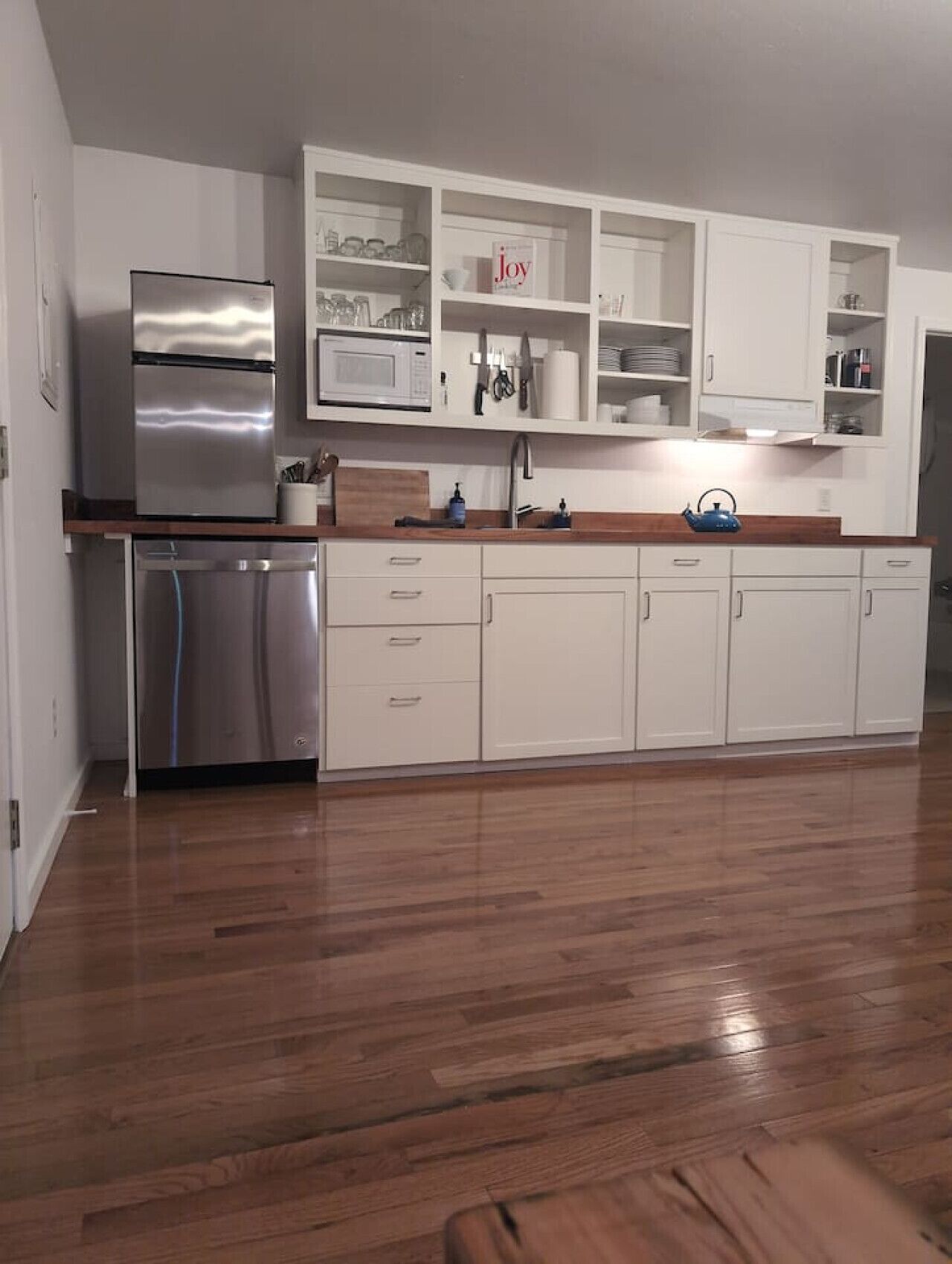 A modern kitchen with white cabinetry, stainless steel appliances, and wooden flooring.