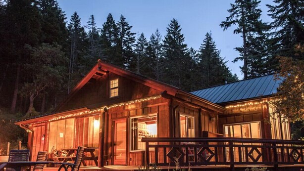 A wooden cabin with a porch, deck, and string lights. - Best Location in Oakridge: Lake and Mountain Views (Oakridge)