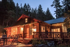 A wooden cabin with a porch, deck, and string lights.