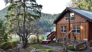 A rustic cabin with a stone foundation, wooden exterior, and a wooden staircase leading to a deck. - Best Location in Oakridge: Lake and Mountain Views (Oakridge)