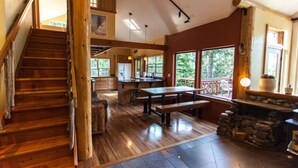 A spacious interior with a wooden staircase, a dining area with a stone fireplace, and large windows offering a view of the outdoors. - Best Location in Oakridge: Lake and Mountain Views (Oakridge)