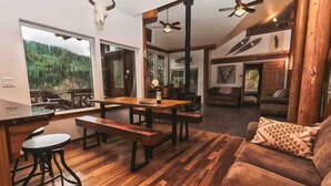 A spacious living area with a wooden floor, a sofa, a dining table with benches, and a kitchen area visible through an open doorway. - Best Location in Oakridge: Lake and Mountain Views (Oakridge)